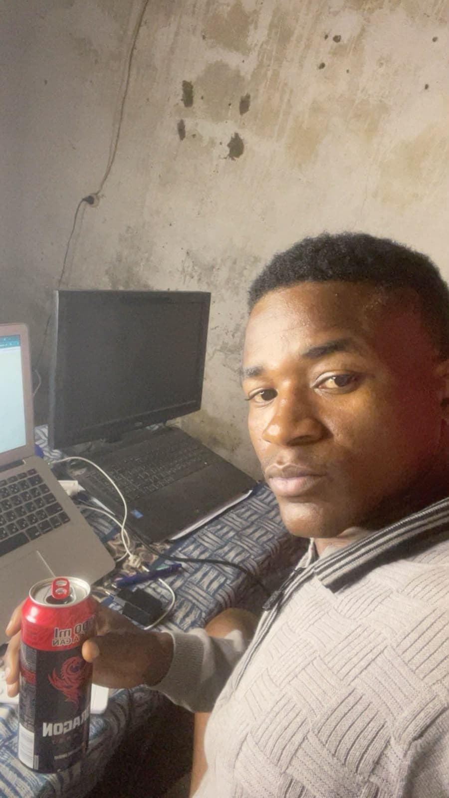 Michael sentado na cama, com dois computadores encostados numa parede de cimento